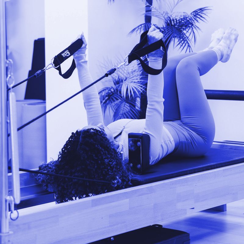 Joana deitada no reformer, a mostrar um exercício com as correias